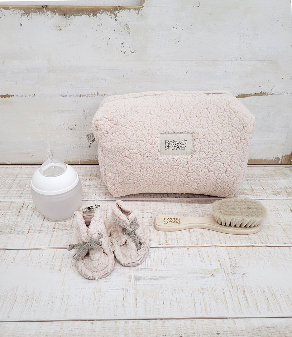 Trousse de toilette bébé maternité en mouton blanc écru, ici photographiée avec les chaussons de naissance en polaire mouton, un biberon et une brosse à cheveux pour bébé. Babyshower, made in Europe.
