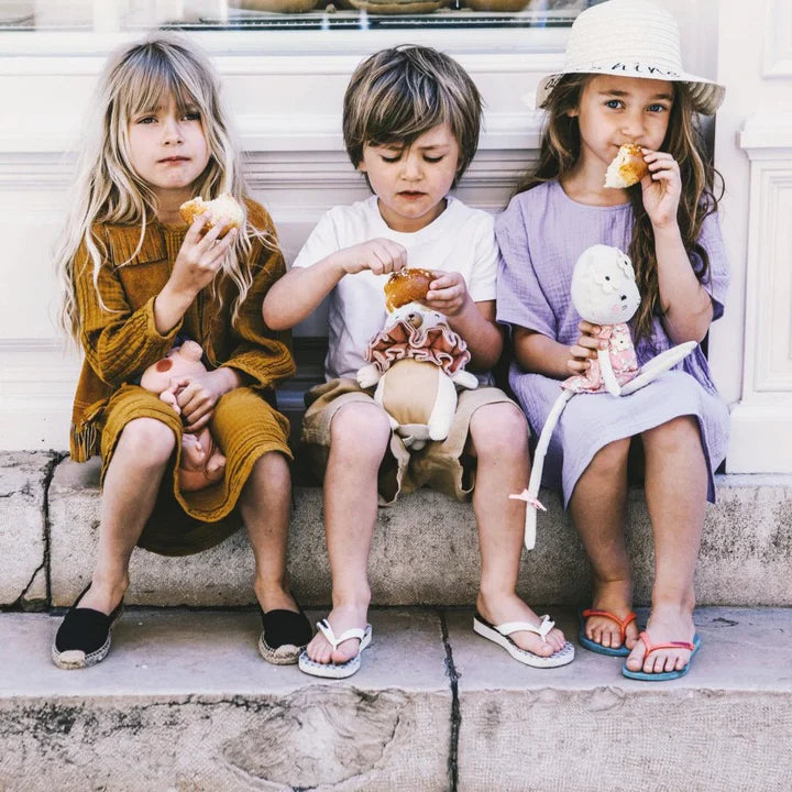 Picca Loulou, des peluches faciles à manipuler et à transporter. Sur la photo, 3 enfants assis sur des marches mangent un goûter avec leur peluche en tissu sur les genoux.