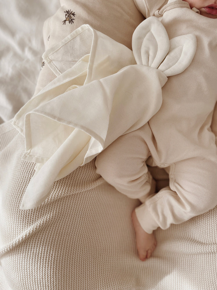 Doudou lange Saga Copenhague délicatement posé à côté d'un bébé faisant la sieste sur une couverture.