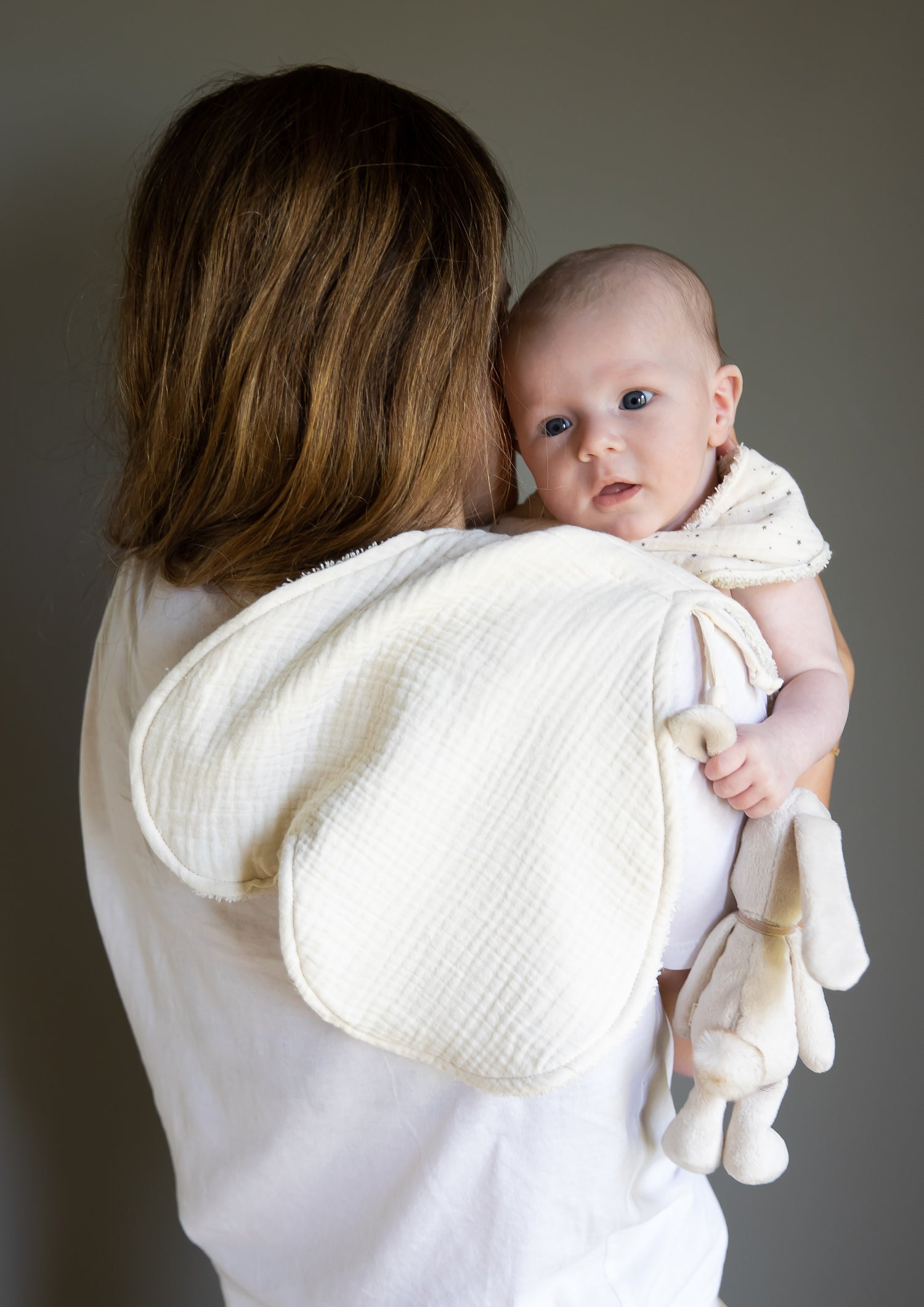 Protège épaule installée sur l'épaule d'une maman en teeshirt blanc qui porte son bébé, tête au dessus de l'épaule.